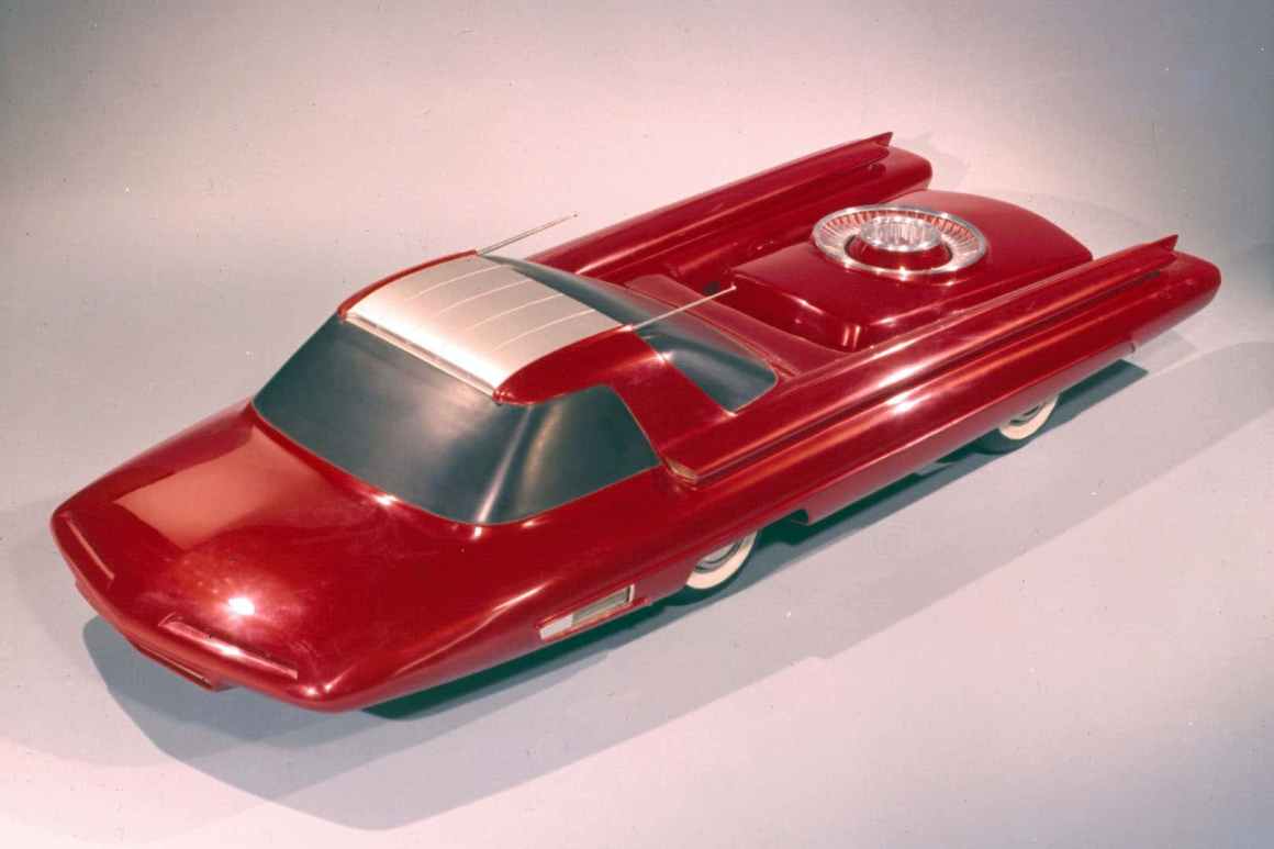 A futuristic red concept car with an aerodynamic design and a metallic roof section, featuring a streamlined body and distinctive tail fins.