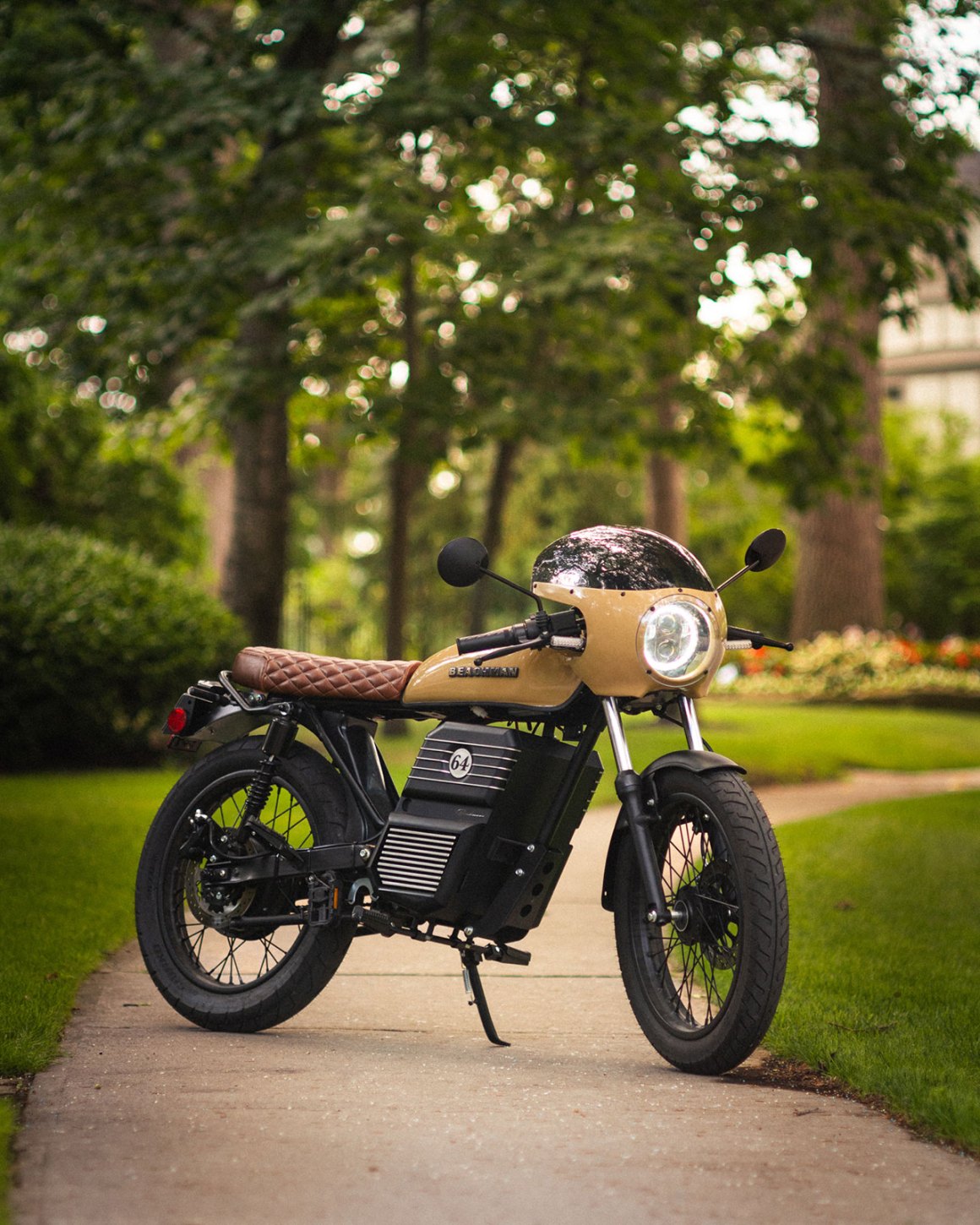 A stylish electric motorcycle with a retro design, featuring a brown leather seat, sleek body, and set against a green park background.
