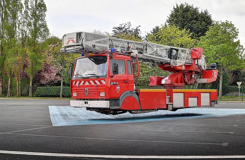 A red fire truck with an extended ladder, parked in a clear area surrounded by trees and greenery.