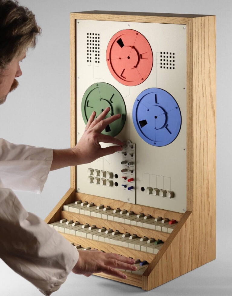 A person in a white coat interacting with a vintage synthesizer featuring colorful circular dials and a set of keys.
