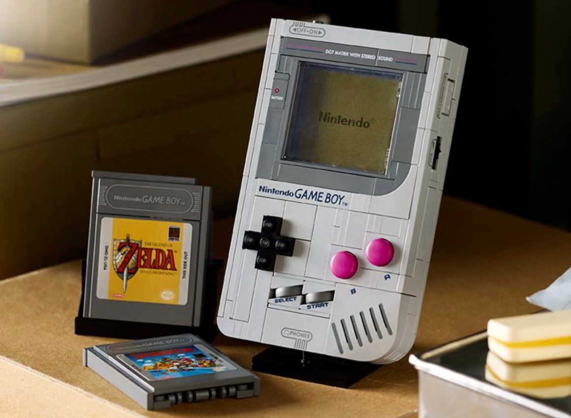 A vintage Nintendo Game Boy console with two game cartridges, one featuring 'The Legend of Zelda' and another showing a colorful game cover, placed on a wooden table.