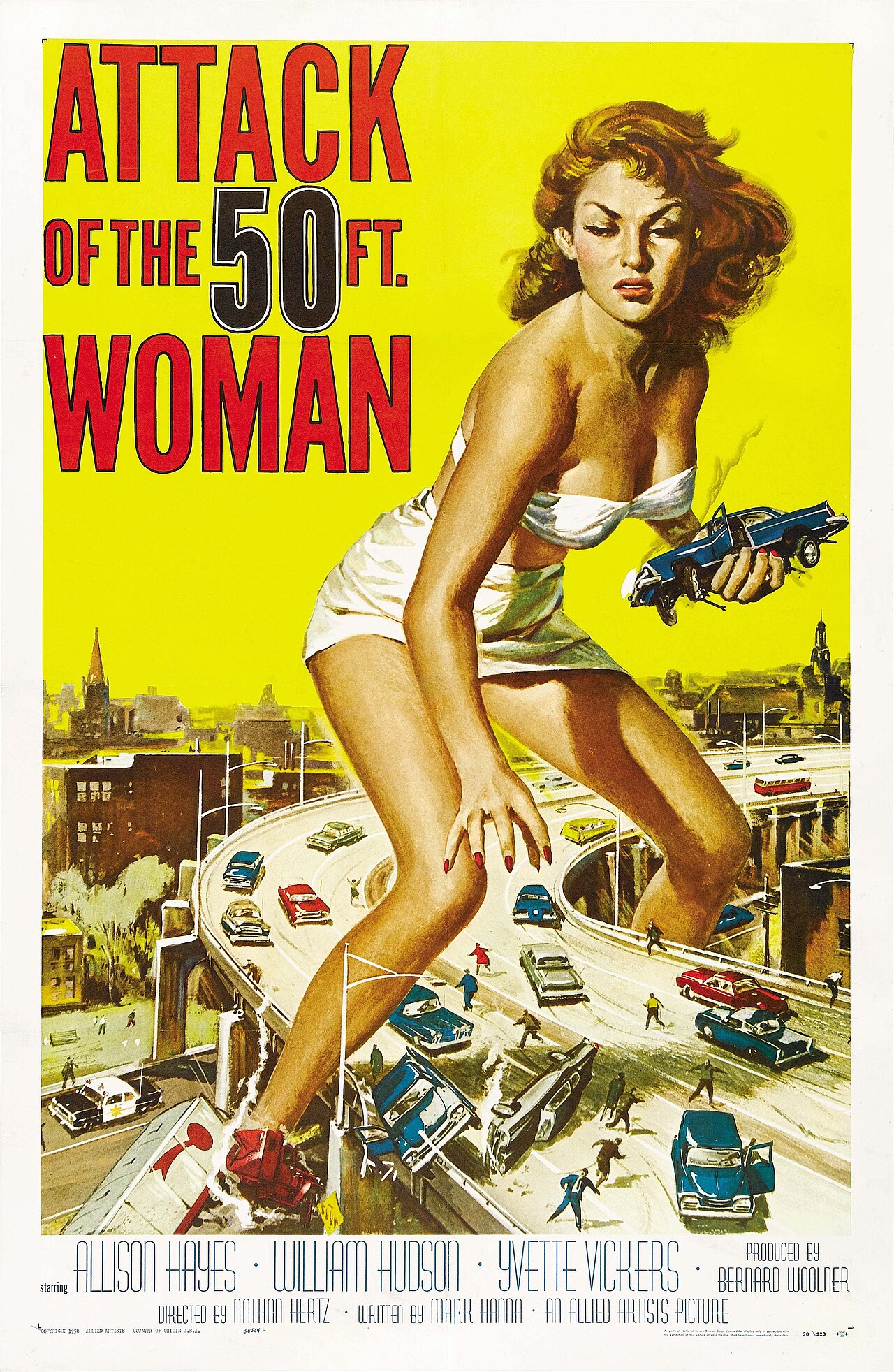 Reynold Brown one-sheet poster for Attack of the 50 Ft. Woman from 1958, a giant Allison Hayes in a white wrap straddling a cloverleaf highway interchange and lifting a car in one hand, tiny cars and people below and a city skyline behind, bold red stacked title on a cream background