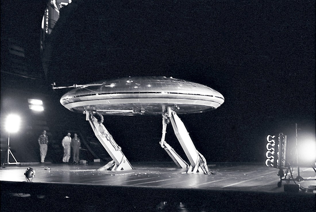 Black and white NASA photograph from March 1960 of the silver, disc-shaped Avrocar mounted inside the enormous Ames wind tunnel, with three technicians beneath it