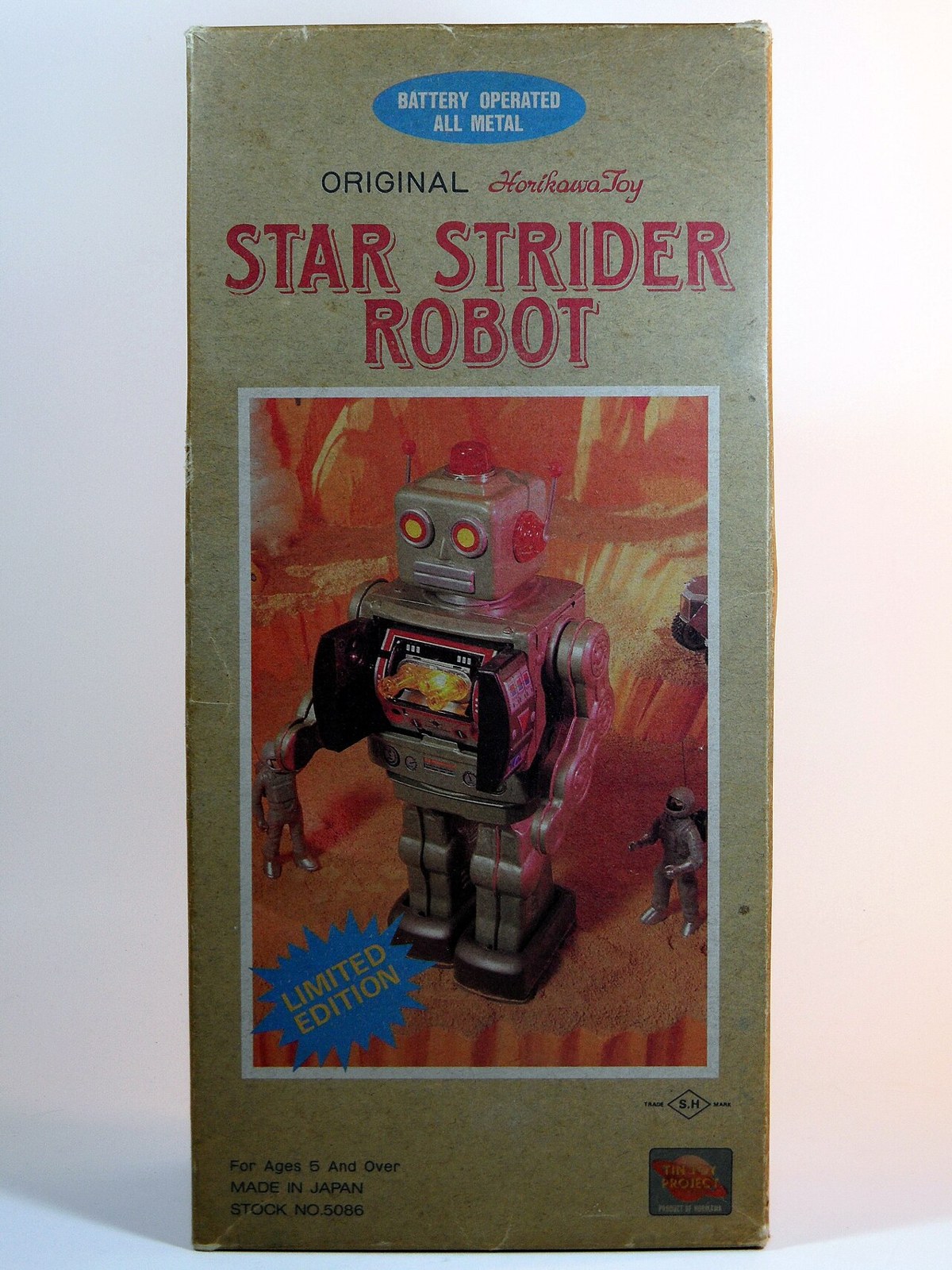Box for the Horikawa Star Strider Robot, a battery operated tin toy, with box art of a gray robot with a glowing chest screen striding across an orange alien landscape under the title in red letters