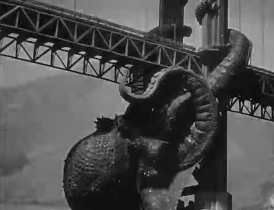 Black and white trailer frame from It Came from Beneath the Sea, a giant octopus with a bulbous body and thick tentacles wrapped around a tower of the Golden Gate Bridge beneath its steel truss deck